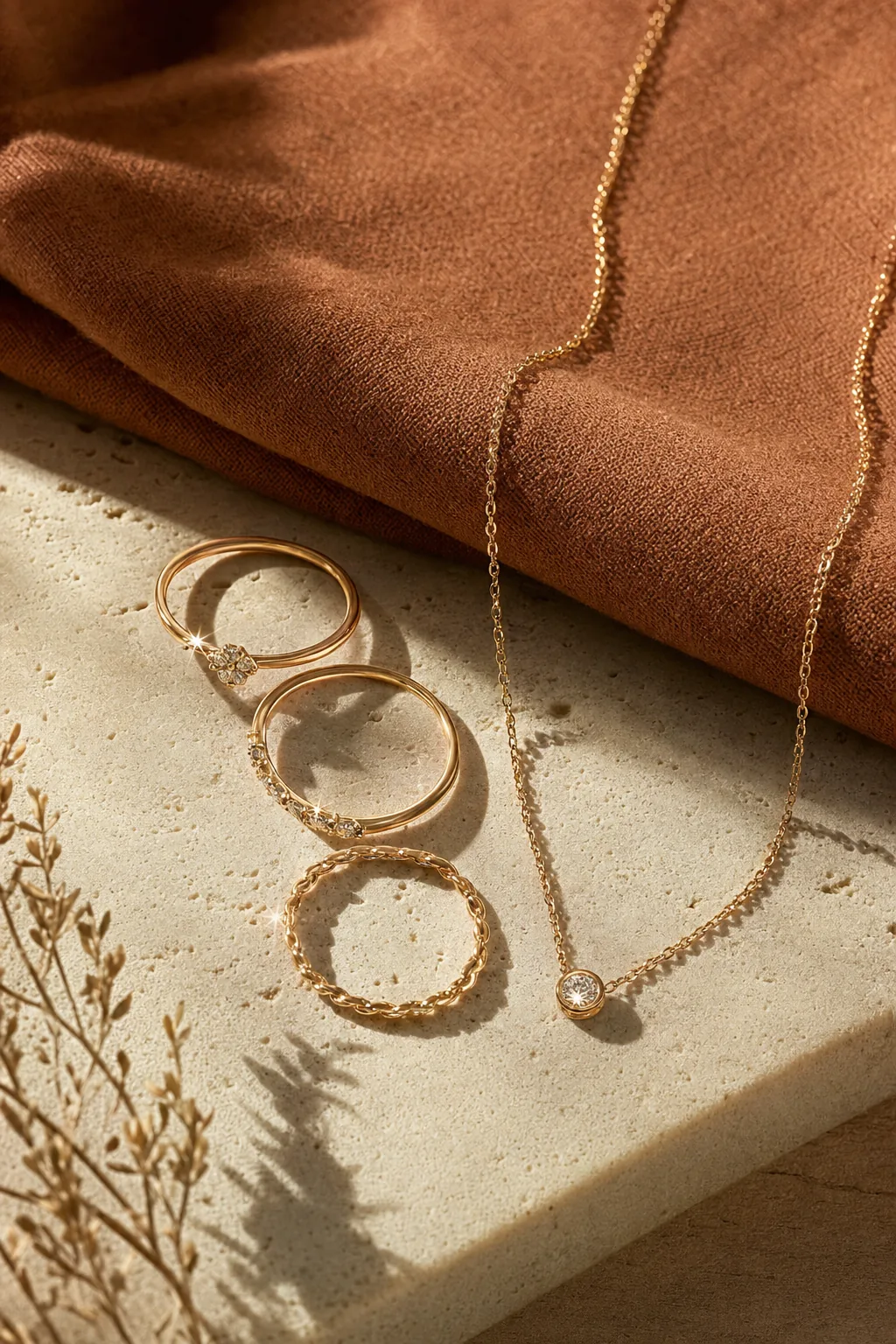 Handcrafted gold rings and a fine chain necklace on a cream stone plinth with terracotta linen
